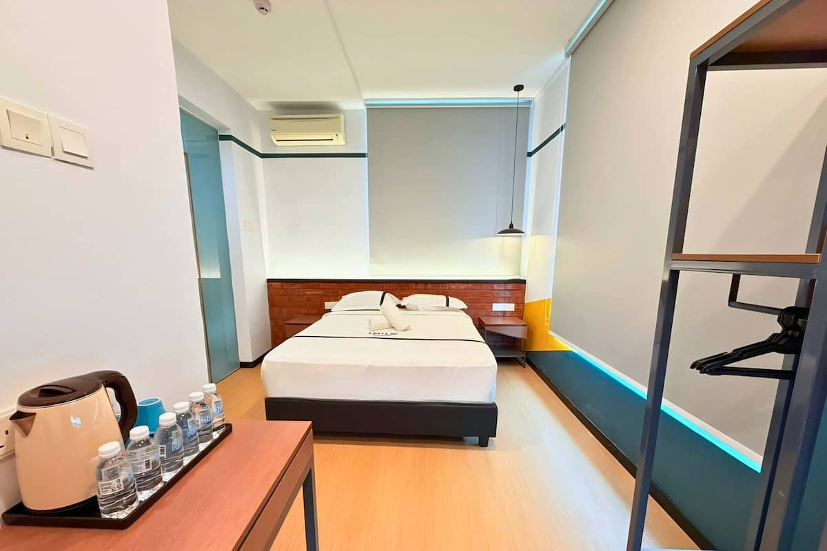 Camera d'albergo con un letto, un comodino con bottiglie d'acqua, un bollitore, una lampada a sospensione e un appendiabiti.
