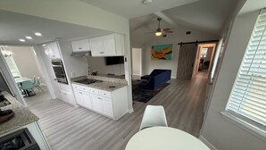 Una cocina moderna con armarios blancos, encimera de granito y horno empotrado. Hay una zona de comedor con una mesa blanca y cuatro sillas.