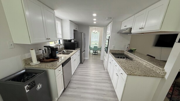 Una cocina moderna con armarios blancos, encimeras de granito, lavavajillas, cafetera y refrigerador.