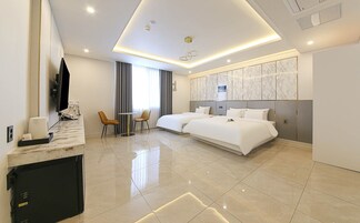 Una habitación de hotel moderna con una cama grande, un escritorio con televisor de pantalla plana, una pequeña zona de estar y un ventanal con cortinas.