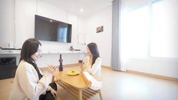 Ein modernes, minimalistisches Zimmer mit einem Holztisch, zwei Stühlen, einem flachbildfernseher an der Wand und einem großen Fenster mit Vorhängen.