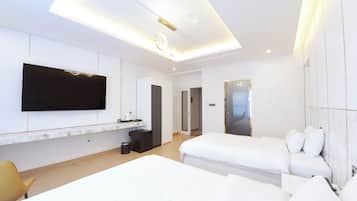 A modern hotel room with a large flat-screen TV mounted on the wall, a small kitchenette, two beds, and a separate bathroom.