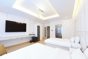 Una habitación de hotel moderna con un televisor de pantalla plana grande montado en la pared, una pequeña kitchenette, dos camas y un baño separado.