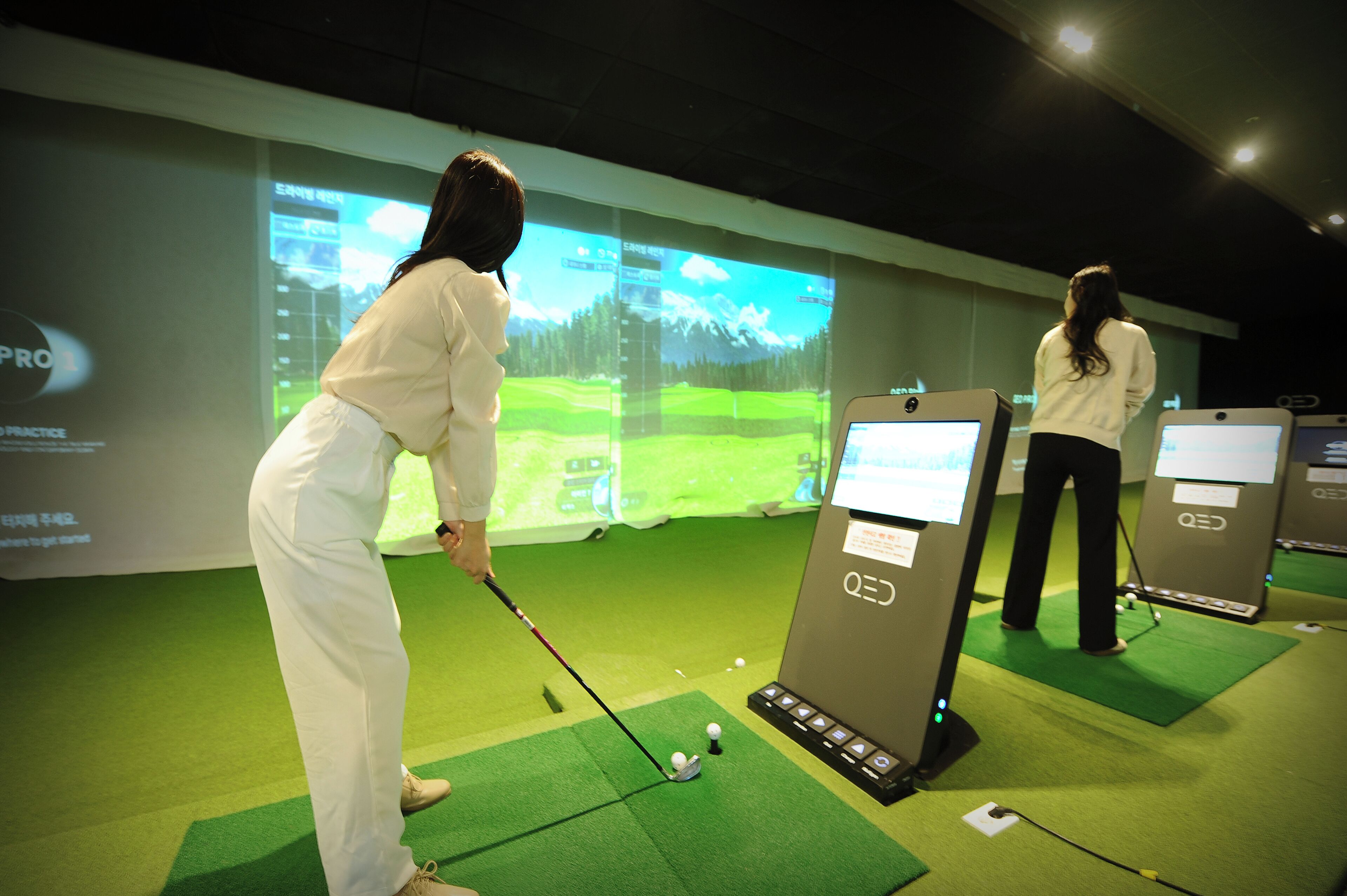Configuración de simulación de golf con pantallas mostrando un campo de golf, un palo de golf y una pelota sobre un tapete.