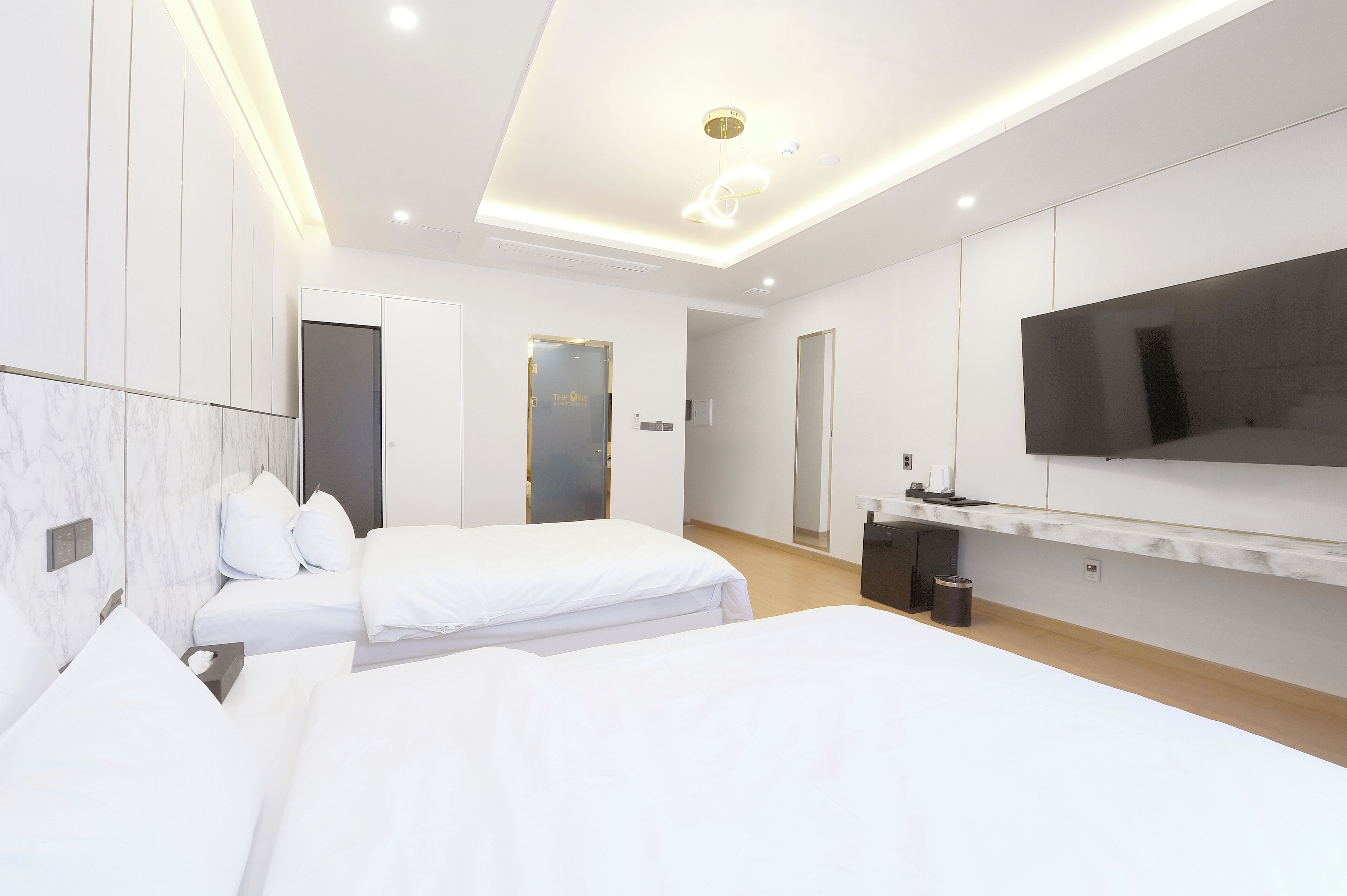 A modern hotel room with two beds, a flat-screen TV mounted on the wall, and a small desk area.