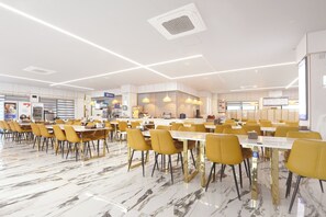 Un amplio comedor con suelo de mármol y sillas amarillas, con una cocina moderna al fondo.