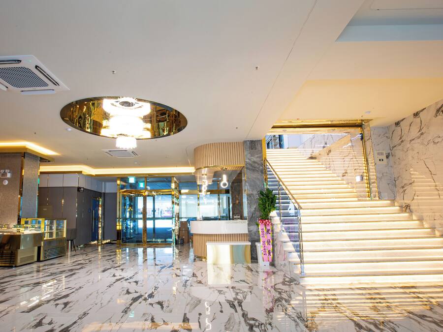 A modern hotel lobby with a marble floor, a reception desk, a staircase, and a large circular light fixture.