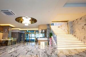 Un moderno vestíbulo de hotel con suelo de mármol, mostrador de recepción, una escalera y una gran lámpara circular.
