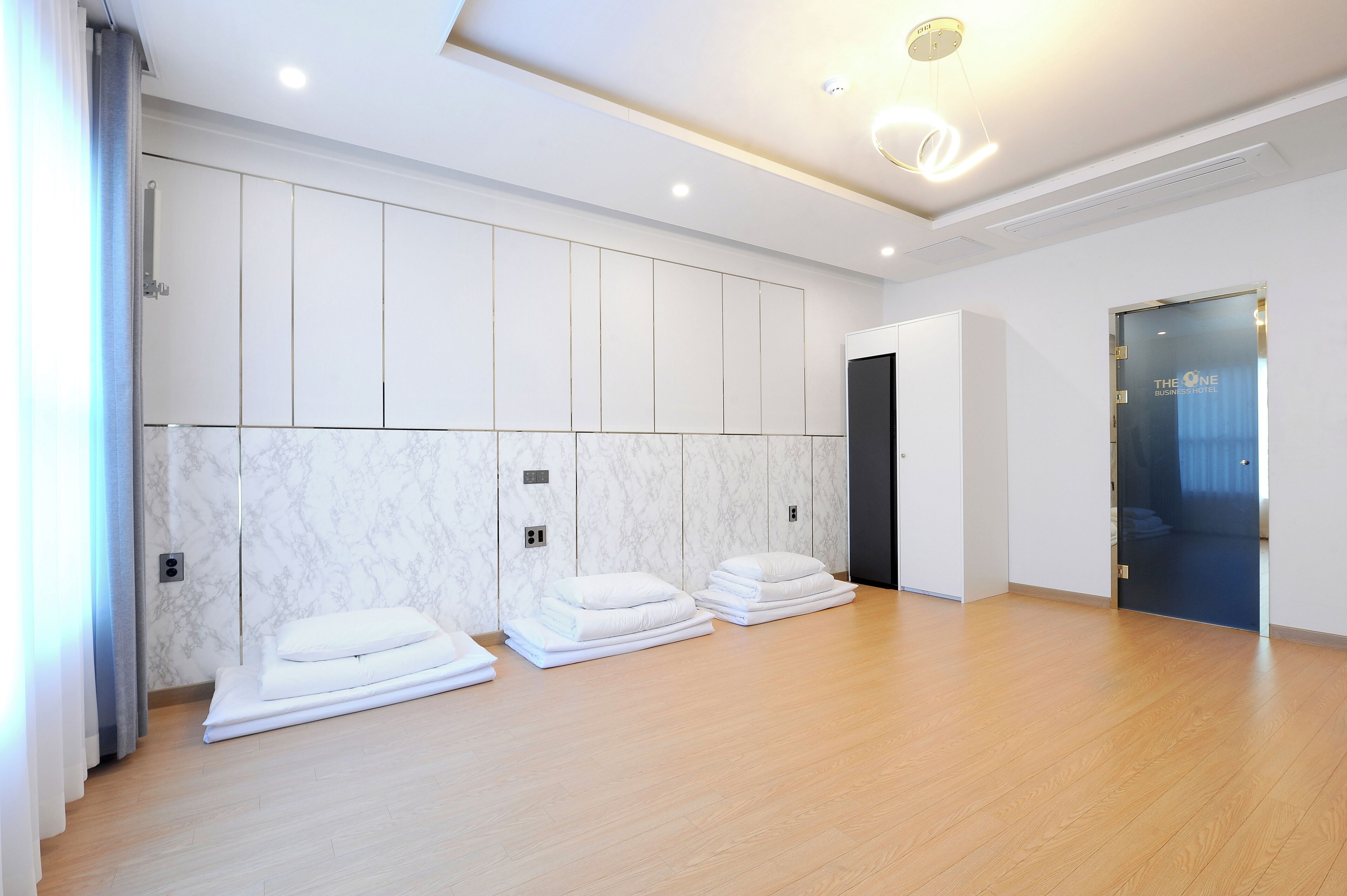 Habitación de hotel con piso de madera, paredes blancas y una pared de acento de mármol. Hay toallas apiladas en el piso y una puerta con panel de vidrio.