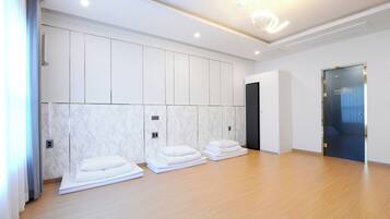 A hotel room with a wooden floor, white walls, and a marble accent wall. There are towels stacked on the floor and a door with a glass panel.