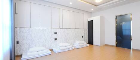 Habitación de hotel con piso de madera, paredes blancas y una pared de acento de mármol. Hay toallas apiladas en el piso y una puerta con panel de vidrio.