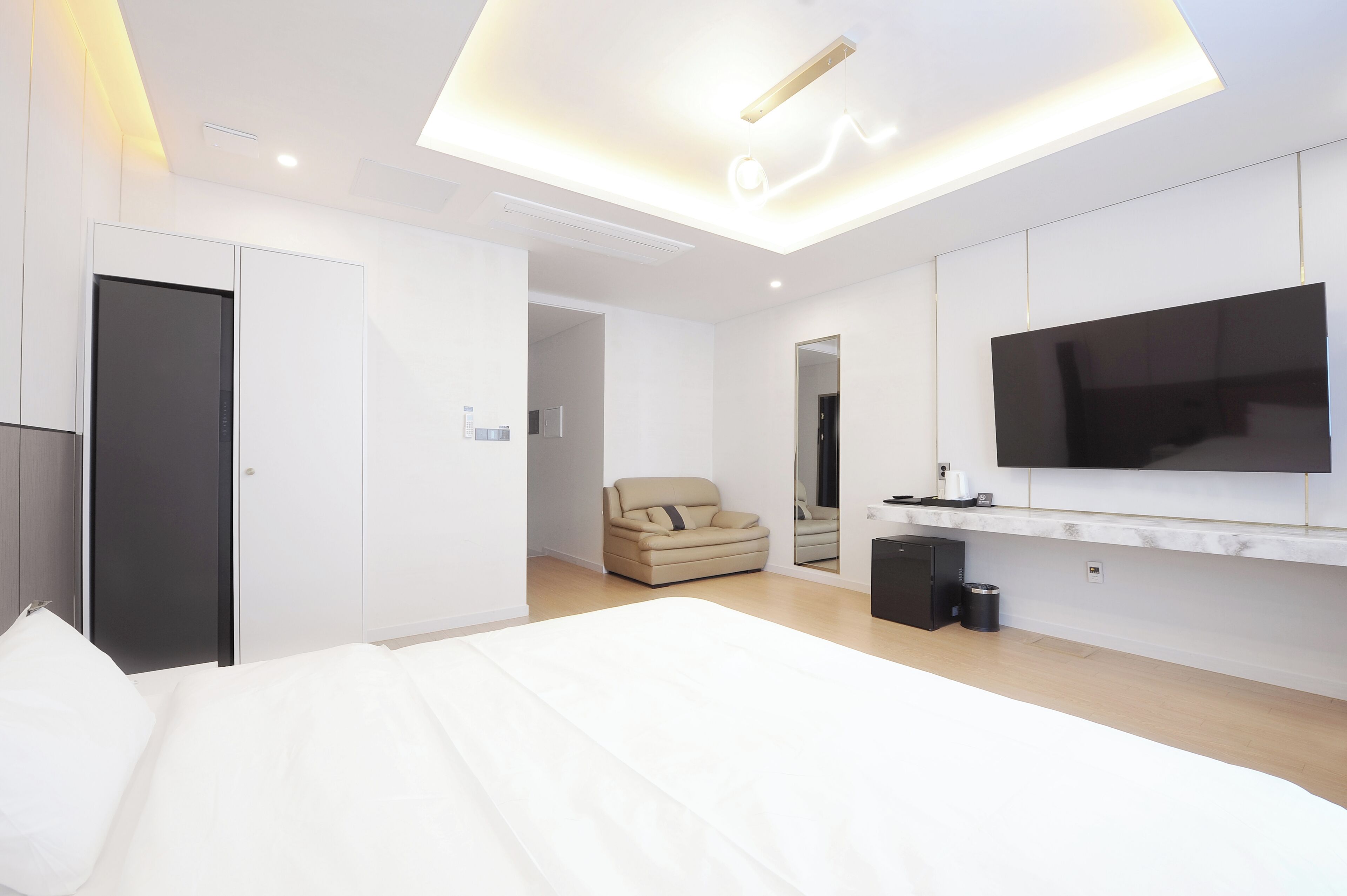 Een moderne slaapkamer met een groot bed, een flatscreen televisie aan de muur en een plafondlamp.