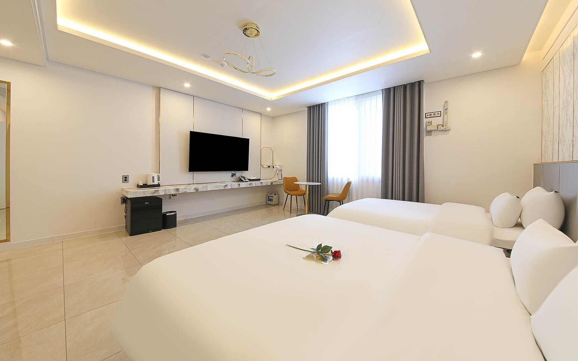 A hotel room with two beds, a desk with a flat-screen TV, a small table with chairs, and a window with curtains.