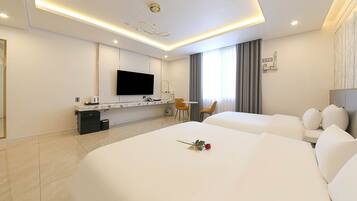 A hotel room with two beds, a desk with a flat-screen TV, a small table with chairs, and a window with curtains.