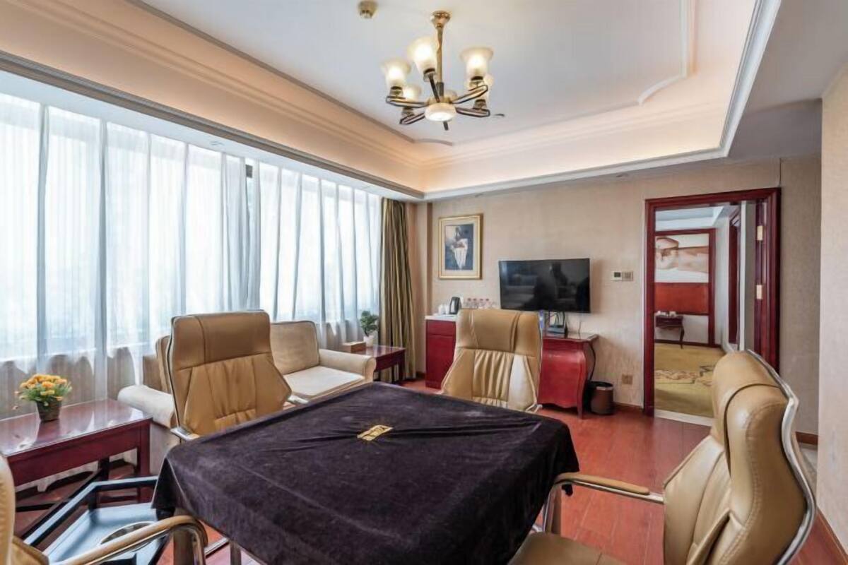 A hotel room with a large bed, a dining table with chairs, a TV, and a desk.