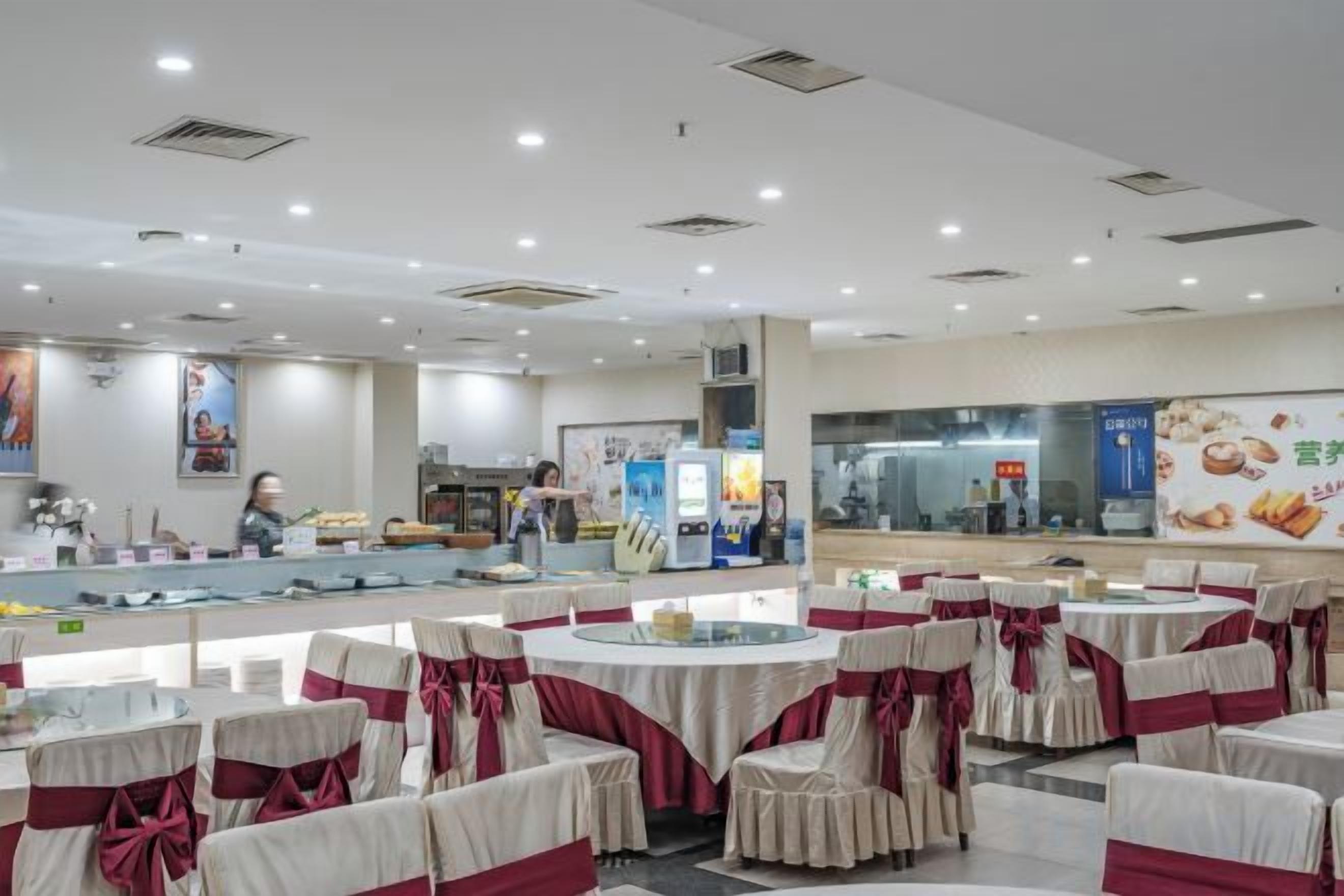 A banquet hall with round tables and chairs, a counter with food display, and a person in the background.