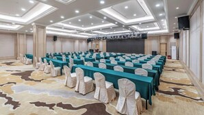 A conference room with rows of tables and chairs, a stage with a projector, and a patterned carpet. - Vienna International Hotel (Foshan Shiwan Hotel Creative Industry Park Branch) (Foshan)