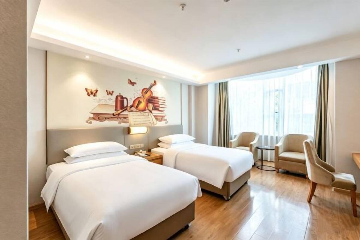 A hotel room with two beds, a mural on the wall, a small table, and a chair.