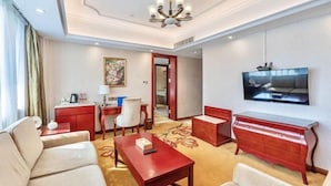A hotel room with a sofa, a red coffee table, a TV mounted on the wall, and a desk with a chair. - Vienna International Hotel (Foshan Shiwan Hotel Creative Industry Park Branch) (Foshan)