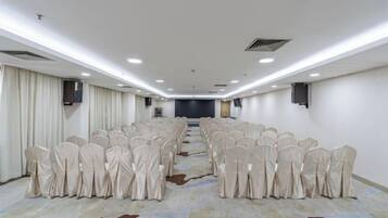 Un salón de conferencias con filas de sillas, piso alfombrado y un escenario al frente.