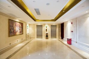 A hotel corridor with a polished floor, a large painting on the left, and two elevators. - Vienna International Hotel (Foshan Zemu Temple Metro Station Lingnan Xintiandi Branch) (Foshan)