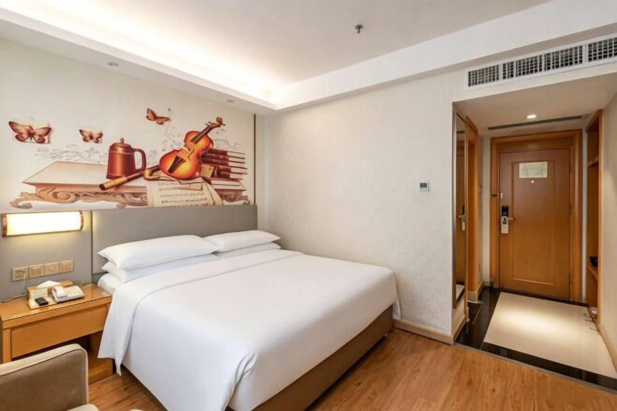 A hotel room with a bed, bedside table, lamp, and a wall mural.