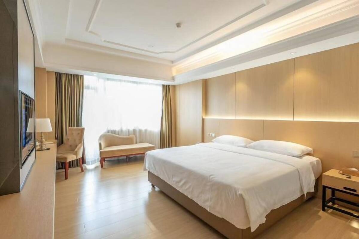 A hotel room with a large bed, a desk, a chair, and a TV.