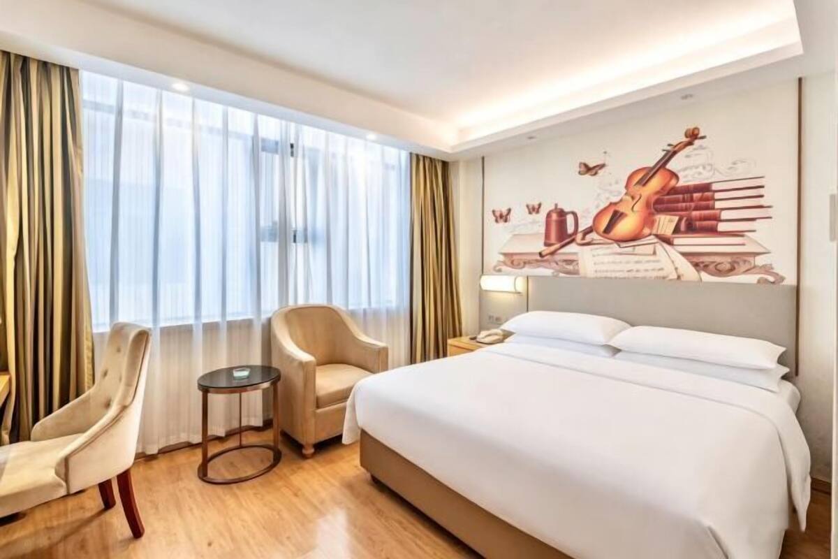 A hotel room with a bed, a chair, a small table, and a wall mural.