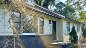 A single-story house with a brick foundation, a front porch, and a small garden area with rocks and plants.