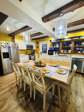 Une cuisine moderne avec des poutres en bois, un îlot central et un coin repas comprenant des chaises et des sets de table.