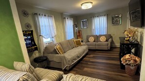 Un salon avec deux canapés, une table basse et un téléviseur. On y trouve des rideaux, des œuvres d’art murales et une petite table ornée de fleurs.