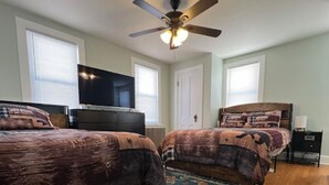 Une chambre avec deux lits, un ventilateur de plafond, une télévision et un tapis à motifs floraux.