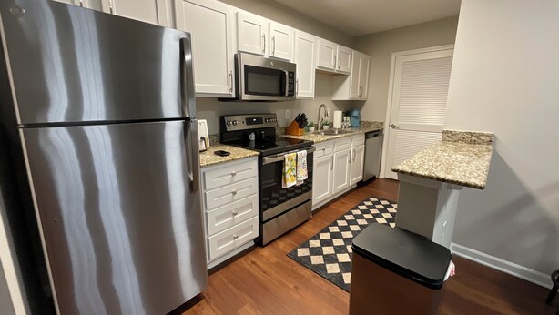 A kitchen with white cabinets, stainless steel appliances, a microwave, and a checkered floor mat. - Charming 2-bedroom apartment in Wilmington, NC (Wilmington)