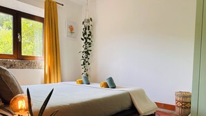 Un dormitorio con cama, mesita de noche, lámpara, planta en maceta y una ventana con cortinas.