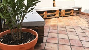 Terraza en la azotea con una maceta, un banco de madera y una pared blanca.