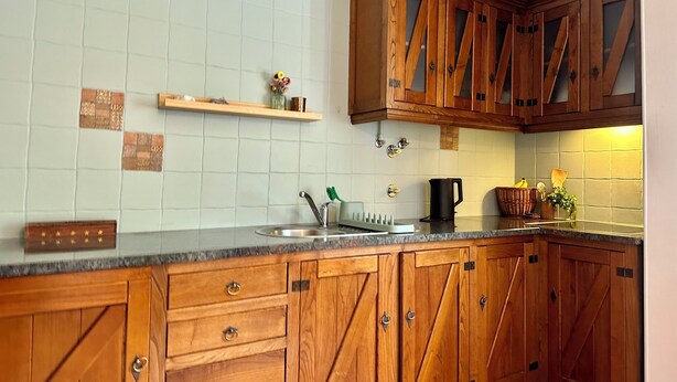 A kitchen with wooden cabinets, a granite countertop, a sink, and a backsplash with square tiles. - Peaceful Sierra Sanctuary (Oliveira do Hospital)