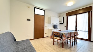 A compact living space with a sofa, a dining table with chairs, a television, and a sliding door leading to a balcony.
