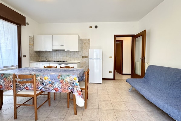 Une cuisine de taille réduite avec des meubles blancs, un réfrigérateur et une table à manger avec des chaises.