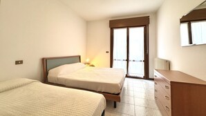 A bedroom with two beds, a dresser, and a sliding glass door to the outside.