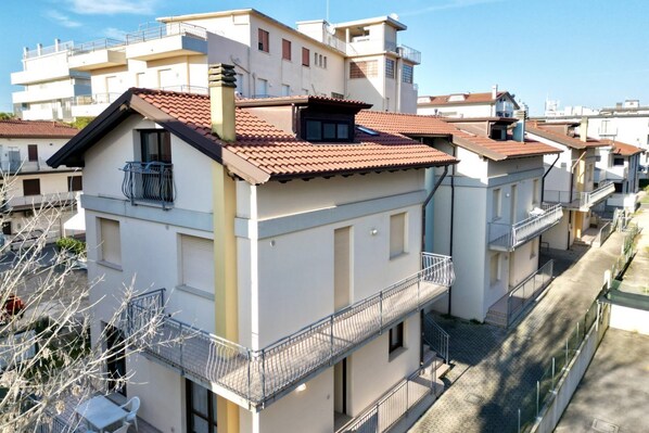 Un edificio residenziale a più piani con balconi, tetto a tegole e cielo sereno.