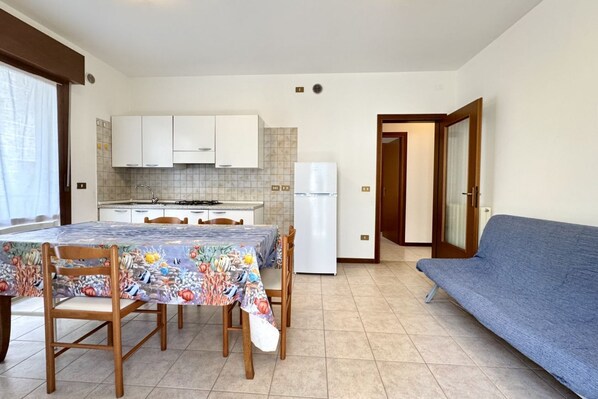 Une cuisine de taille réduite avec des meubles blancs, un réfrigérateur et une table à manger avec des chaises.