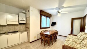 Eine kompakte Küche mit weißen Schränken, einem Esstisch mit Stühlen, einem Deckenventilator und einem an der Wand montierten Fernseher.