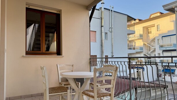 Un balcón con mesa y sillas, una ventana y vistas a edificios cercanos.