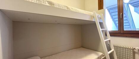 A bunk bed with a ladder, a window with a view of a building, and a radiator.