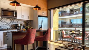 Una cocina moderna con una isla central, taburetes de bar y un comedor con vistas a un balcón.