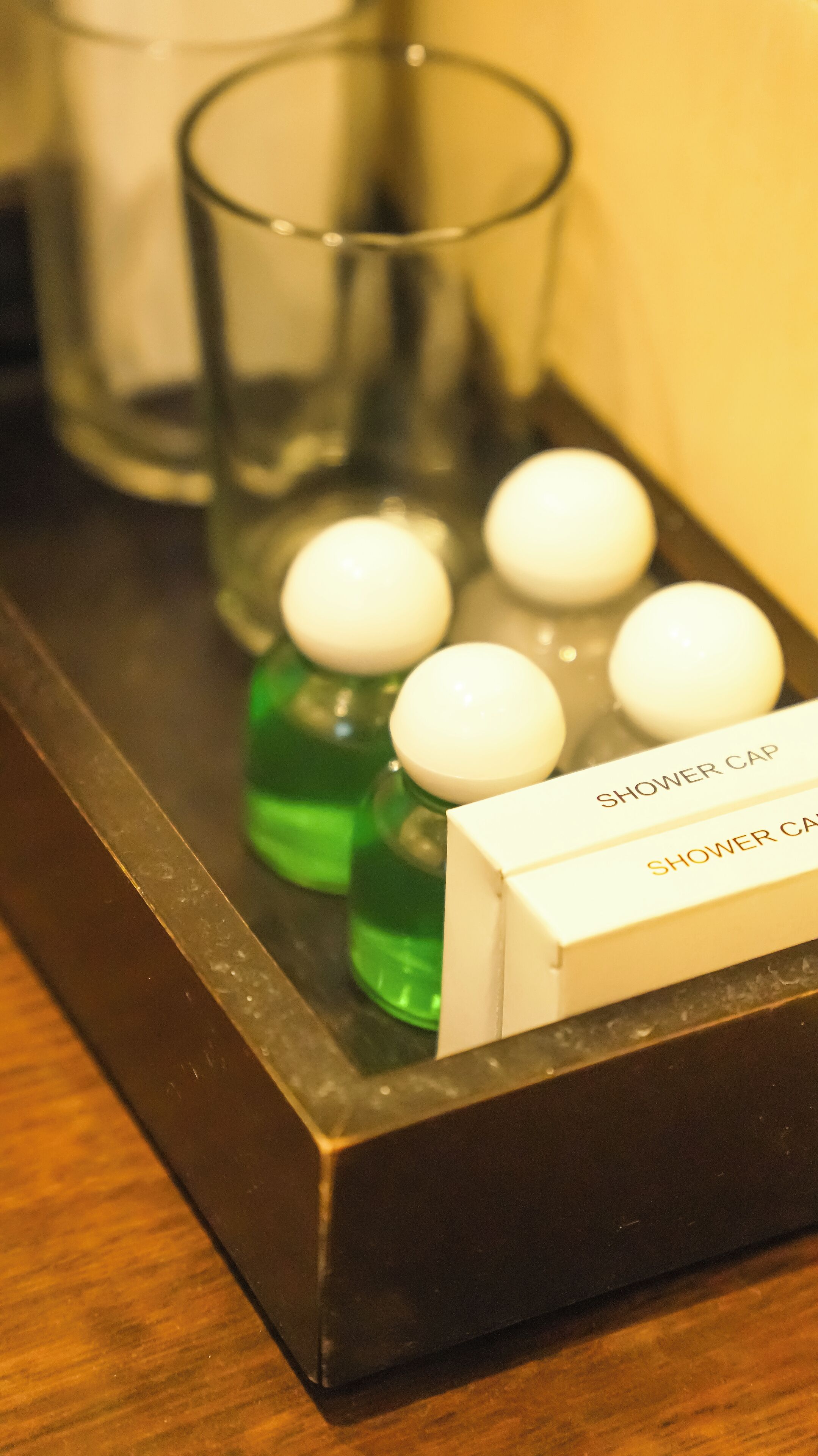 Un plateau contenant quatre bonnets de douche blancs et deux bouteilles vertes, probablement remplies de shampoing ou d’après-shampoing, est posé sur un plateau foncé.