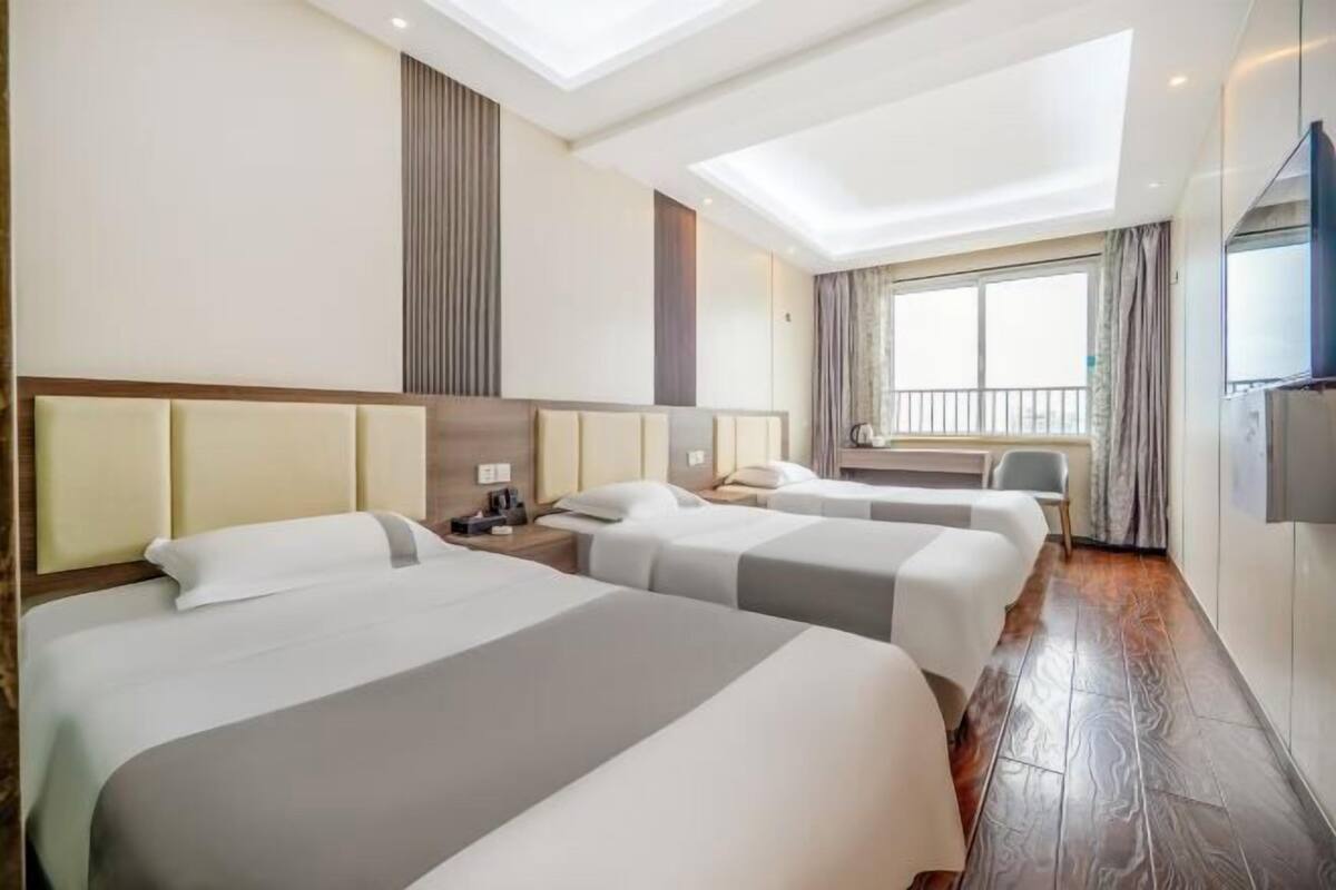A hotel room with three beds, a TV, a desk, and a window with a view.