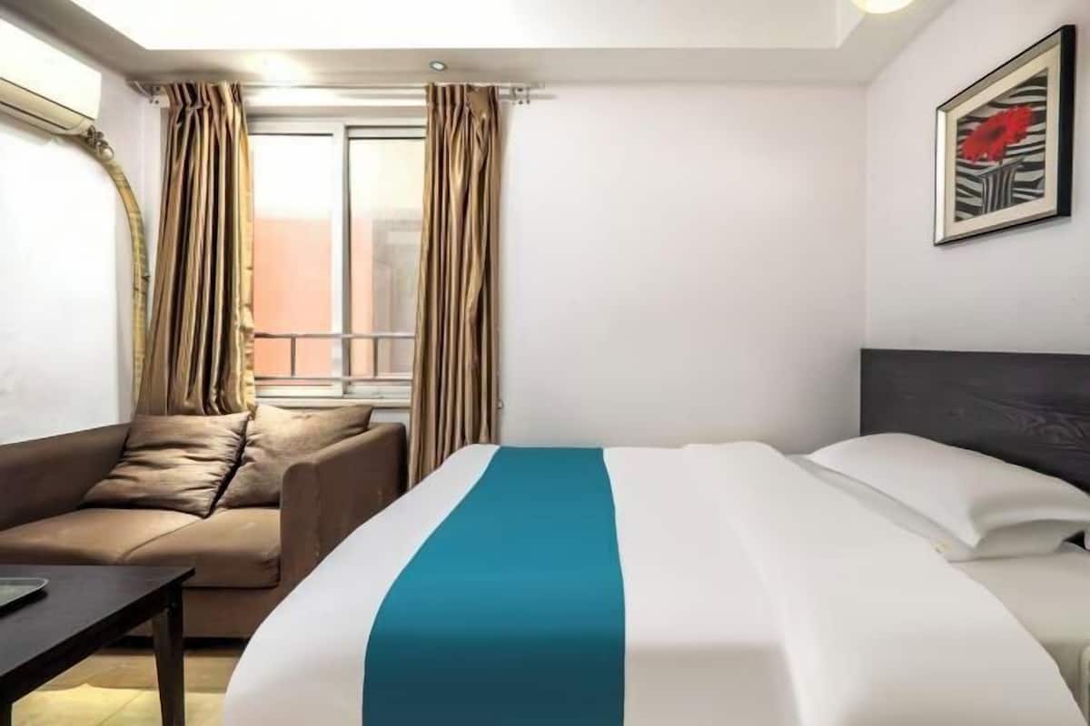 A hotel room with a bed, a sofa, a table, and a window with curtains.