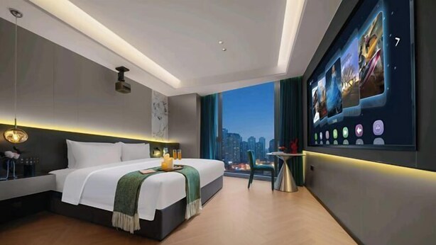 A modern hotel room with a large bed, a city view, a desk with a chair, and a large digital photo display on the wall. - Tiantian Chain Hotel Chongqing Xinan Hospital (Chongqing)