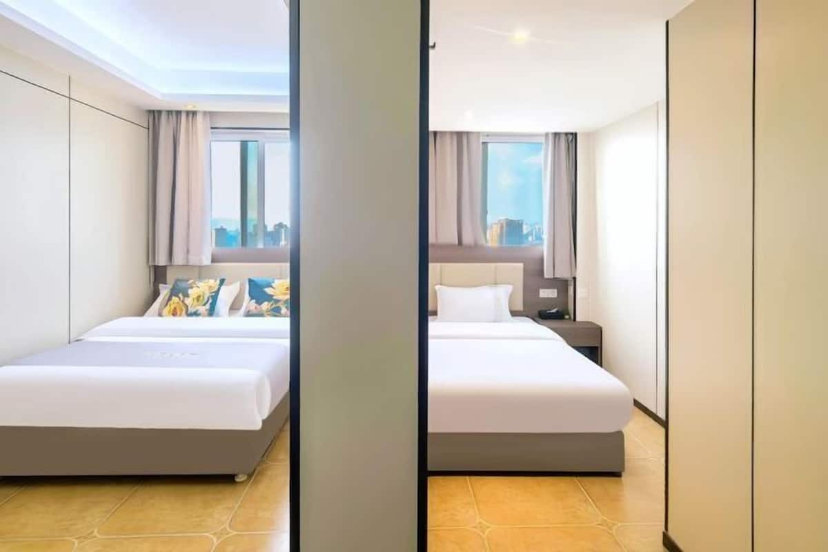 A hotel room with two beds, large windows, and a city view.